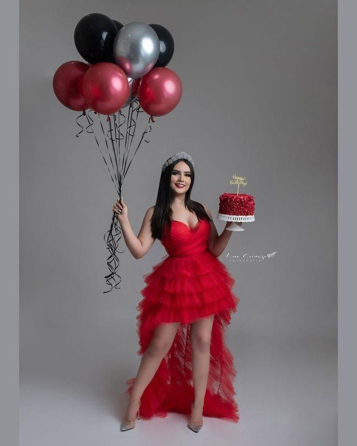 a woman in a red dress holding a cake and balloons