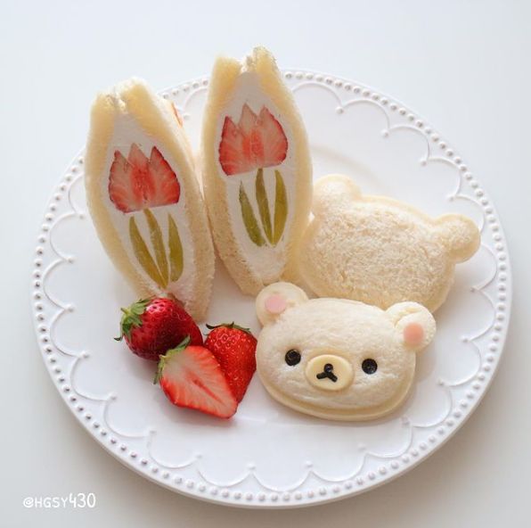 a white plate topped with cut in half sandwiches next to strawberries and a teddy bear