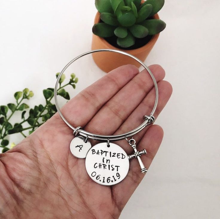 a hand holding a bracelet with two charms on it and a potted plant in the background