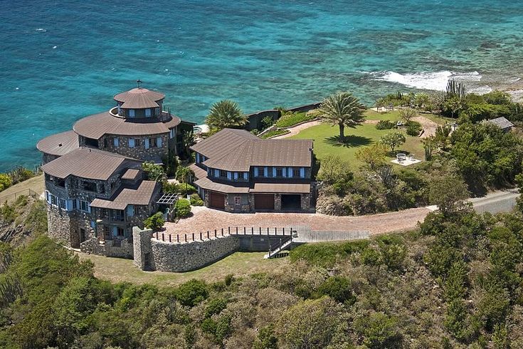 this is an aerial view of a mansion on the ocean shore with blue water in the background