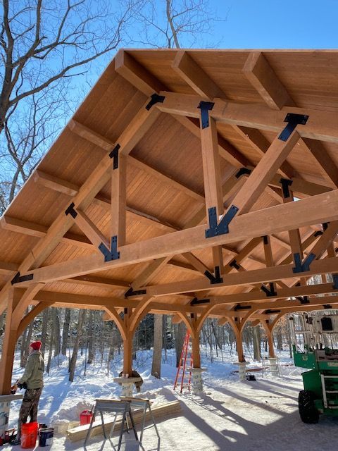 a large wooden structure sitting in the middle of a snow covered forest with people working on it