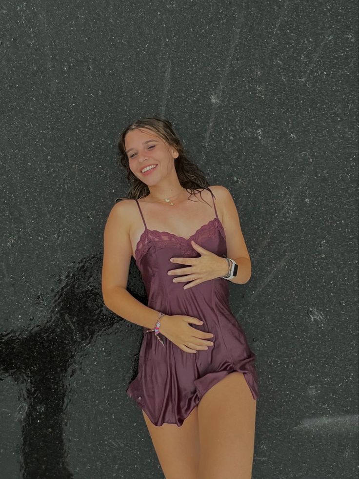 a woman in a purple bathing suit standing next to a black wall with her hands on her stomach