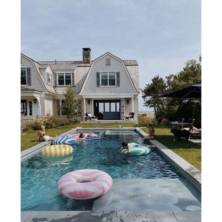 an inflatable pool is next to a large house with people sitting around it