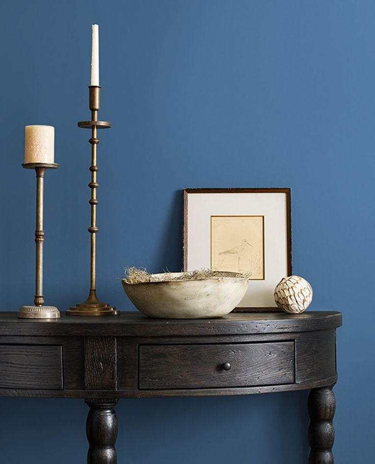 a wooden table topped with a bowl next to a candle and framed pictures on the wall