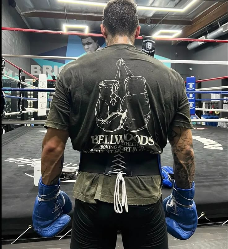 a man wearing boxing gloves standing in a boxing ring with his back to the camera