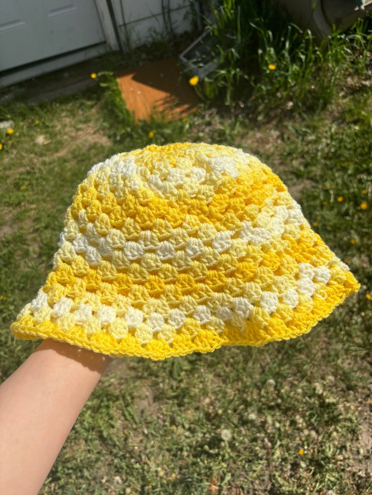 someone is holding up a yellow and white crocheted sunhat in the grass