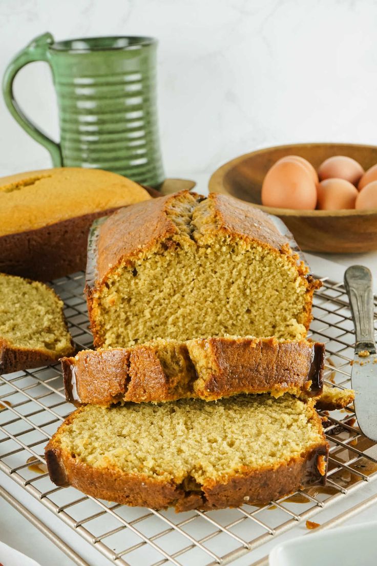 sliced loaf of banana bread sitting on top of a cooling rack next to some eggs