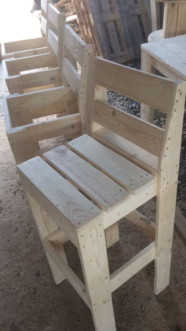 three wooden chairs sitting next to each other on top of a dirt ground with wood pallets in the background