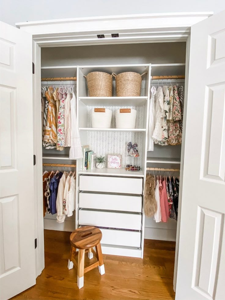 an open closet with clothes and baskets on the shelves, next to a step stool