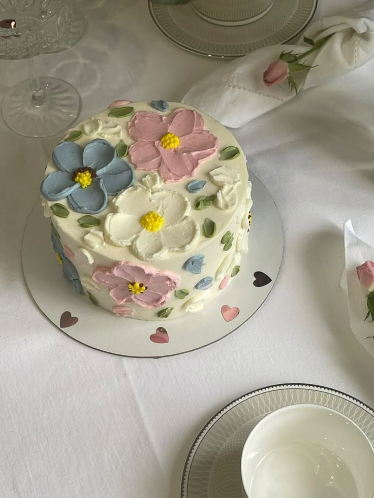 a white table topped with a cake covered in pink and blue flowers next to plates