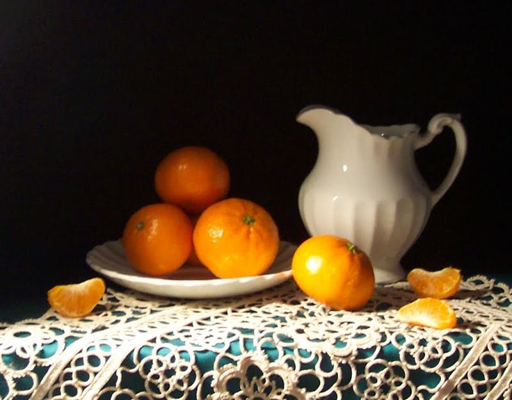 a white pitcher sitting on top of a table next to oranges and a plate