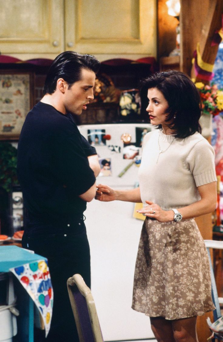 the young man and woman are standing in front of the refrigerator door, looking at each other