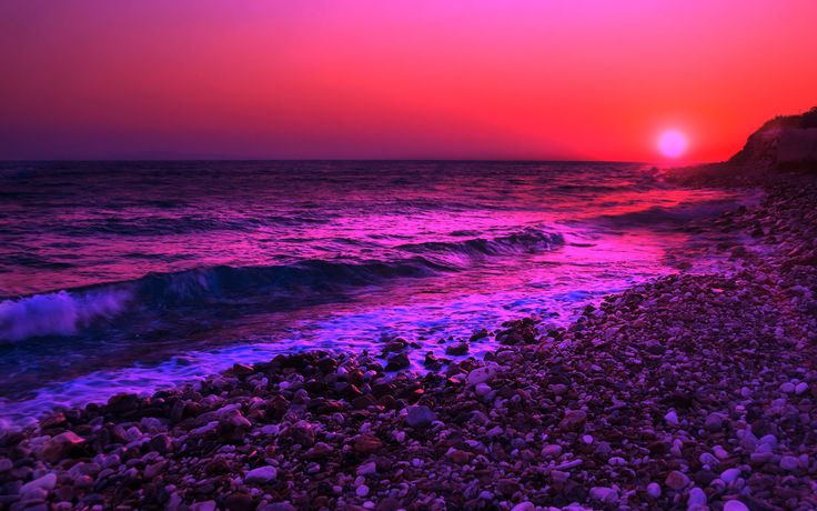 the sun is setting over the ocean with rocks and pebbles on the beach below it