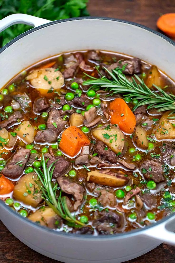 a pot filled with stew and vegetables on top of a wooden table next to carrots