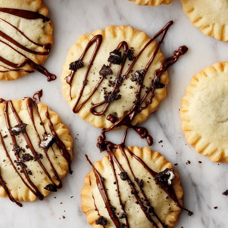 several cookies with chocolate drizzled on them sitting on a marble counter top