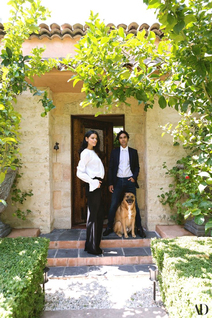 two people standing in front of a door with a dog sitting on the steps next to them