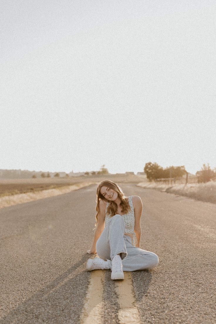 a woman sitting on the side of an empty road