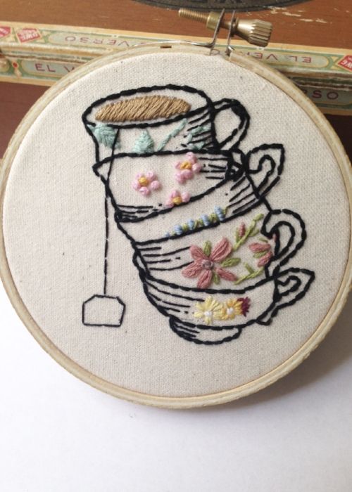 a hand embroidered picture of a teacup with flowers on it and a needle in the middle