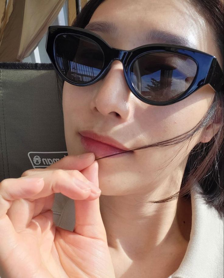 a woman wearing sunglasses and holding a cell phone up to her face while looking at the camera