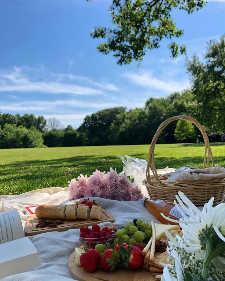 a picnic with fruit, cheese and bread rolls on a blanket in front of trees