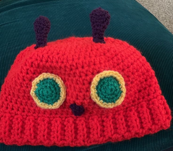 a crocheted red hat with green eyes and ears