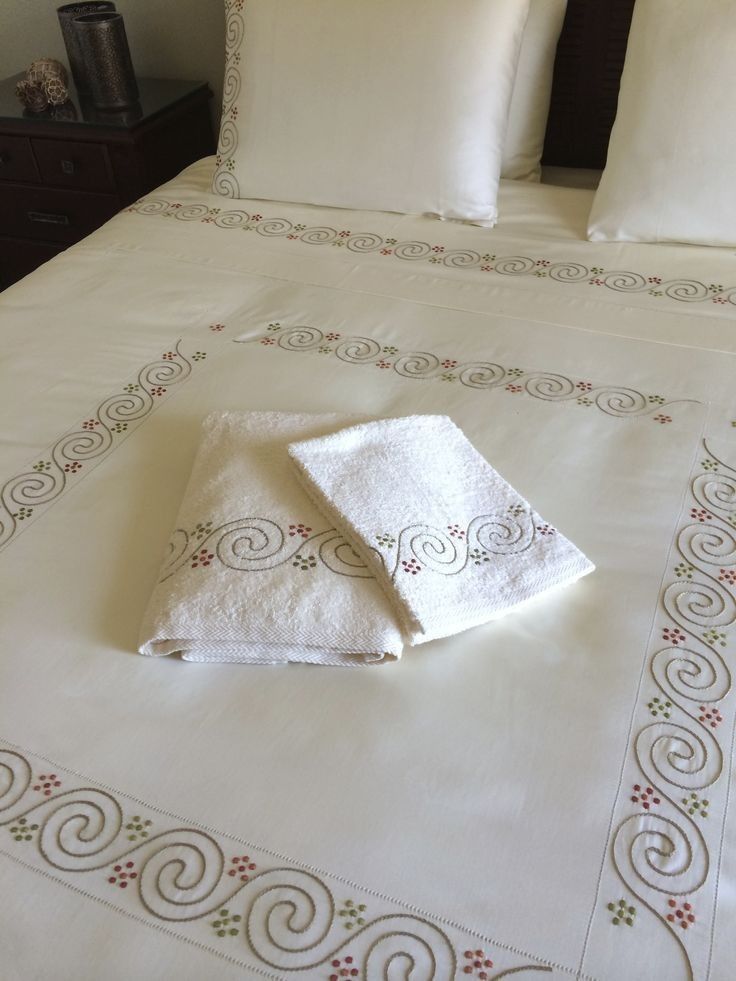 two towels folded on top of a bed with white linens and decorative embroidered border