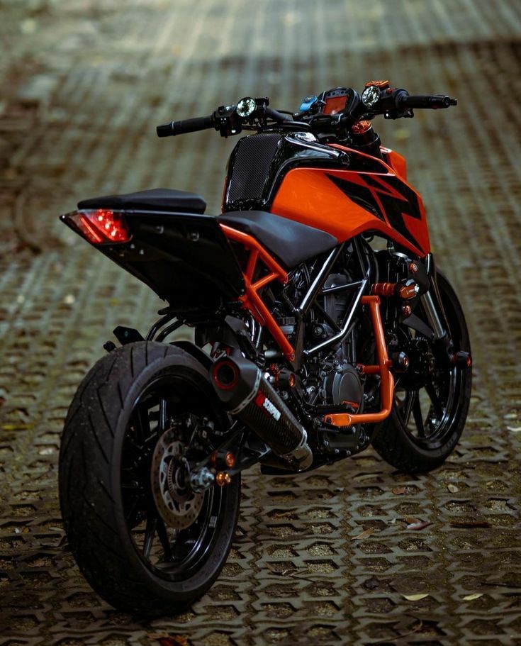 an orange and black motorcycle parked on top of a cobblestone floored area