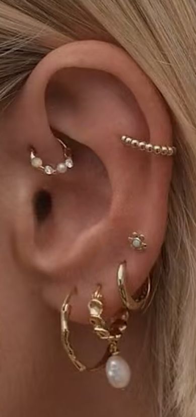 a woman wearing three different types of ear piercings on her left ear and the other one is gold