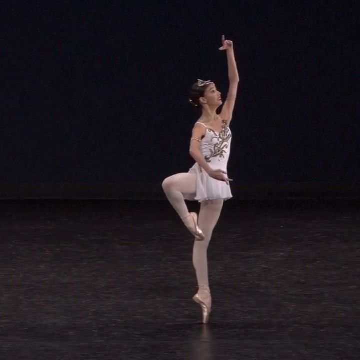 a ballerina in white is doing a ballet move with her arms up and legs apart