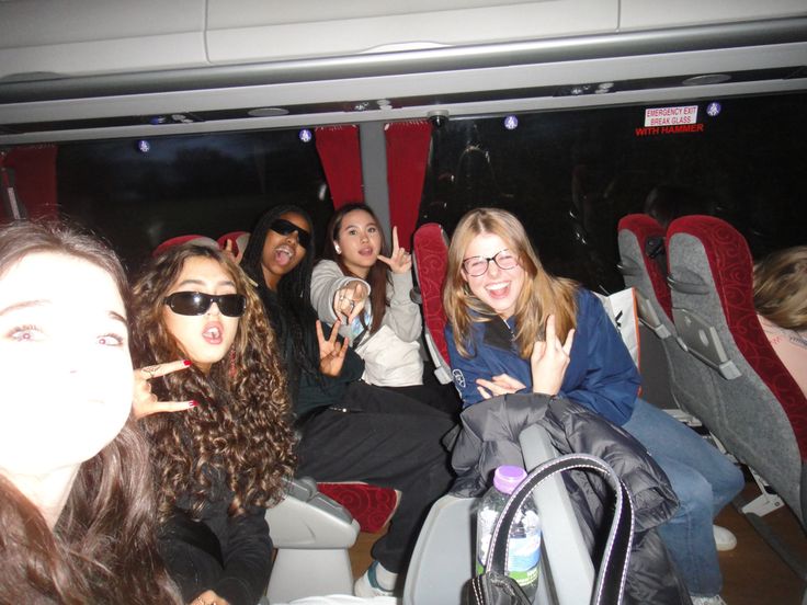 group of young women sitting in seats on bus with one pointing at camera and the other holding up peace signs