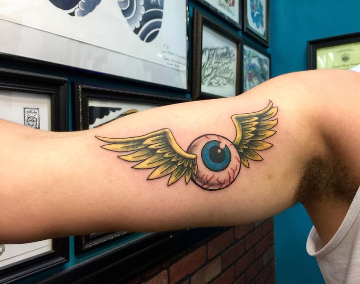 a man's arm with an eyeball and wings tattoo on the left side of his arm