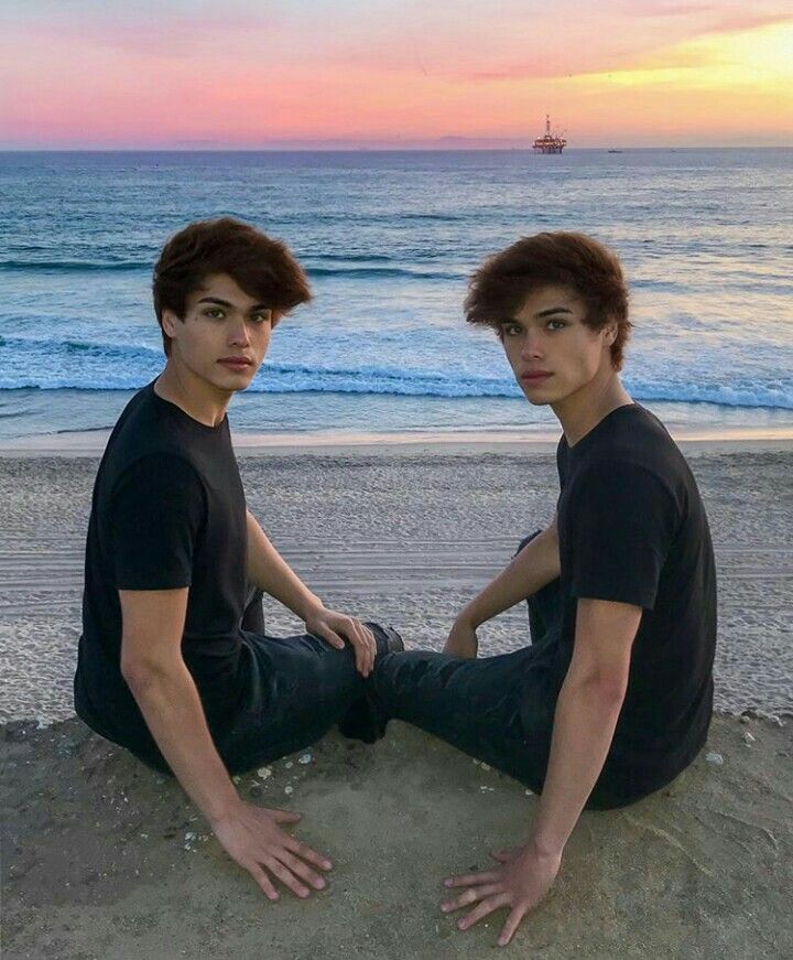 two young men sitting on the beach at sunset