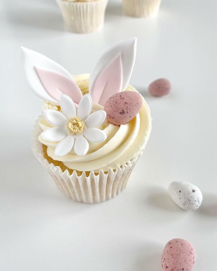 cupcakes decorated with white and pink frosting are sitting on a table next to small speckled eggs