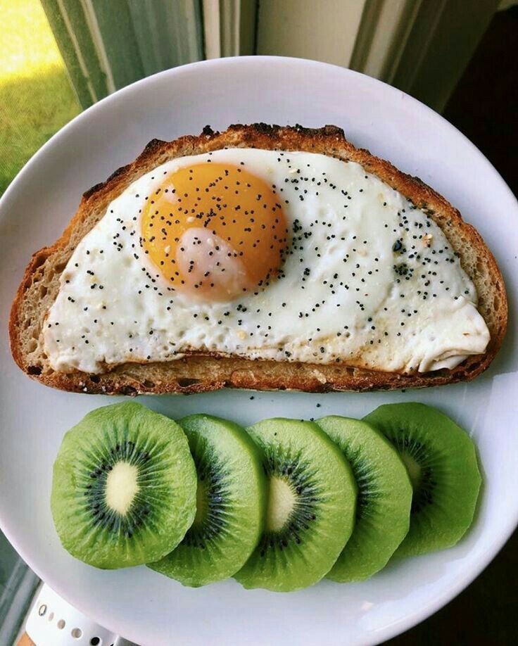 a white plate topped with sliced kiwi and an egg on top of toasted bread