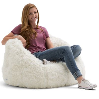 a woman is sitting on a fluffy white bean bag chair with her legs crossed and smiling