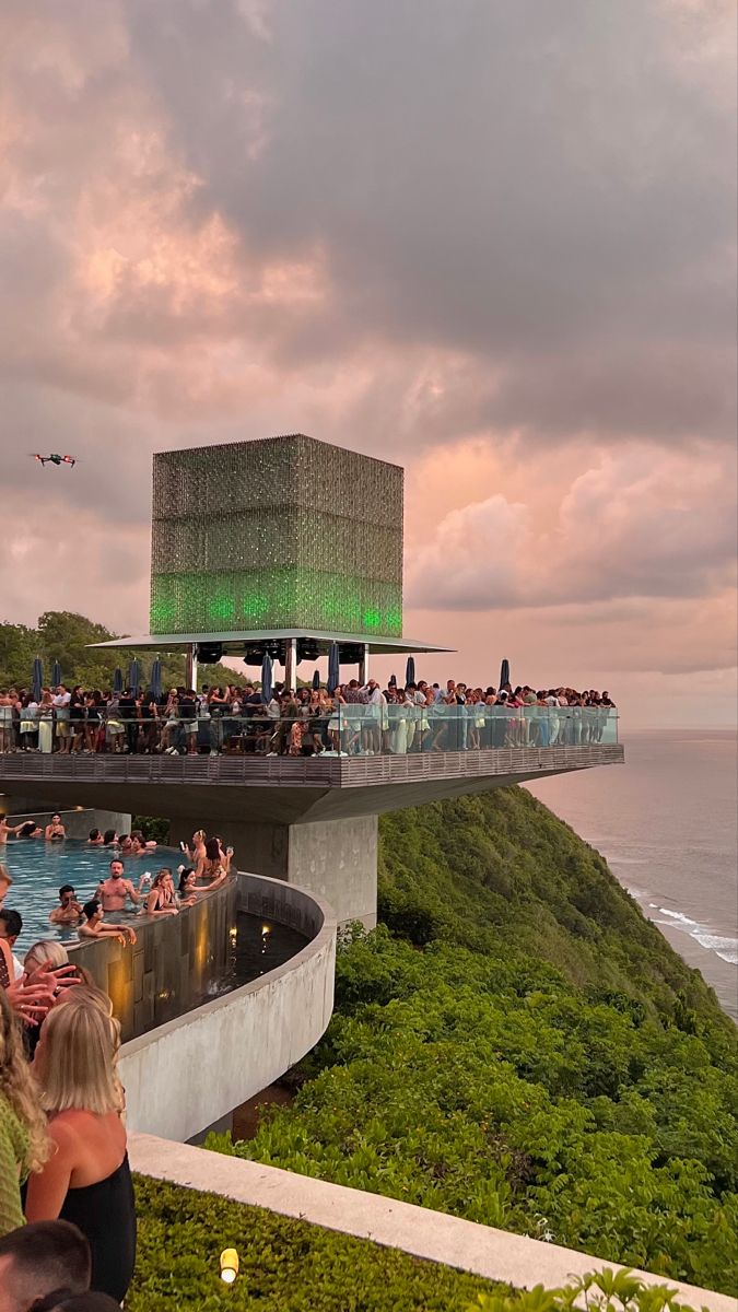 people are sitting in an outdoor swimming pool near the ocean at sunset or sunrise time