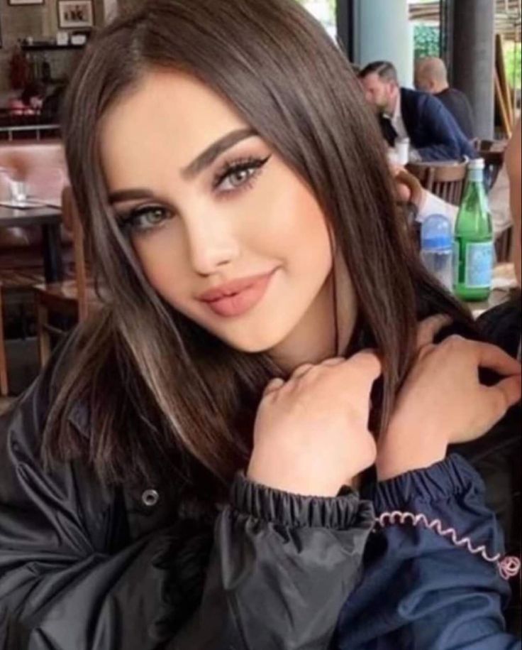 a woman with long brown hair wearing a black jacket and posing for a photo in a restaurant