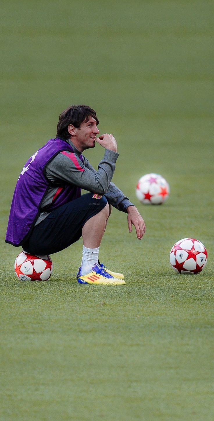 a man sitting on top of a field next to soccer balls