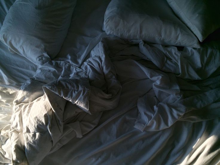 an unmade bed with white sheets and pillows