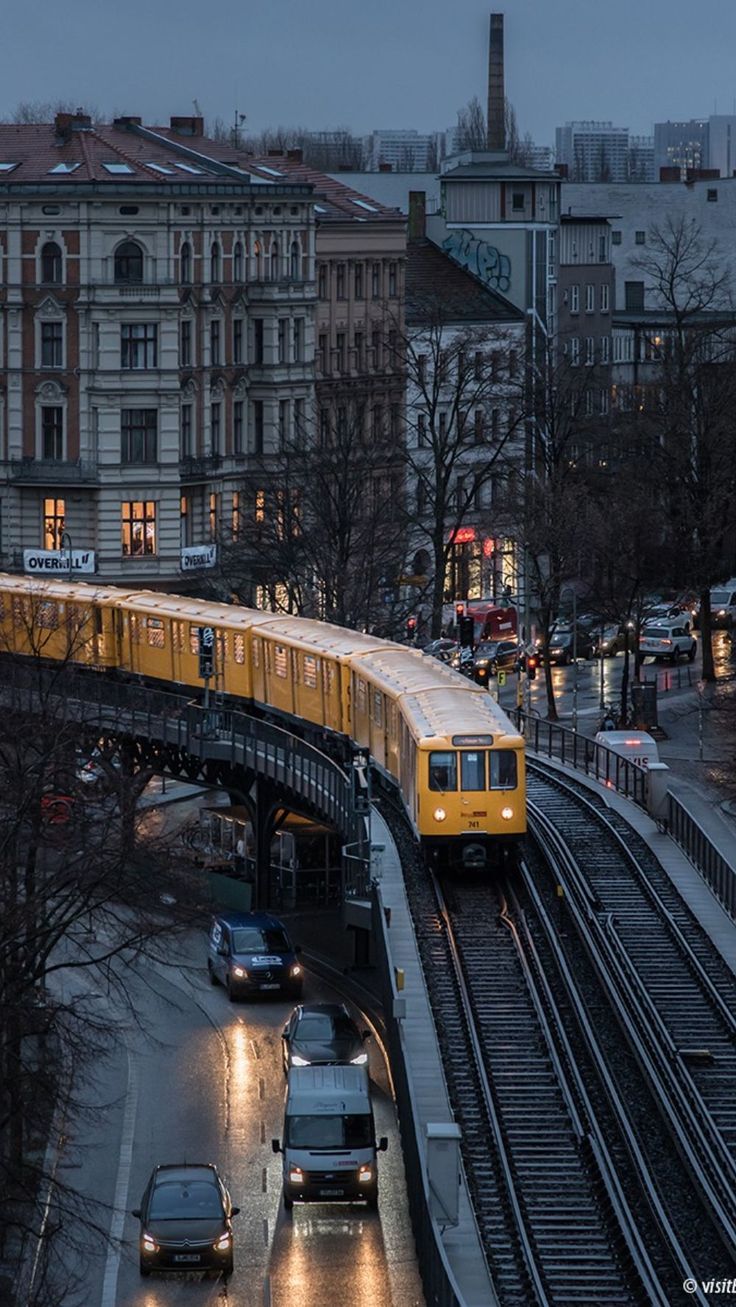 a yellow train traveling over a bridge next to traffic on a street near tall buildings