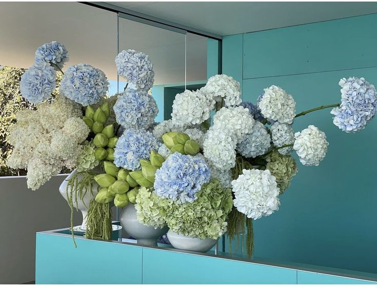 blue and white flowers sit in vases on a counter next to a large mirror