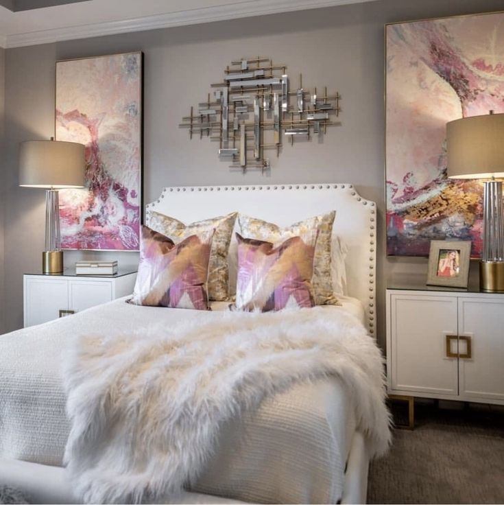 a white bed topped with lots of pillows next to two wall mounted pictures above it