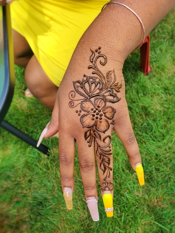 a woman's hand with henna tattoos on it and yellow nail polishes