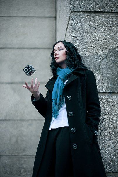 a woman in black coat and blue scarf holding dice