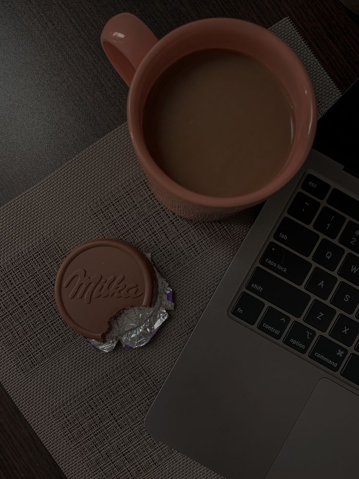 a cup of coffee sitting next to a laptop computer on a table with a chocolate bar