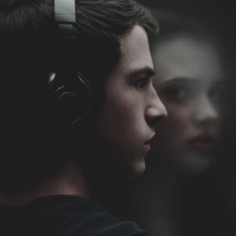 two young men with headphones looking at each other in front of a dark background