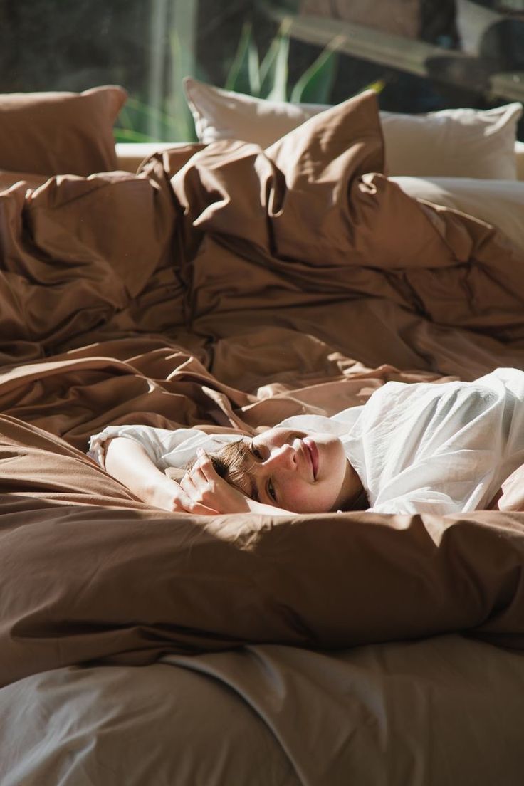 a woman laying on top of a bed covered in brown sheets and pillowcases