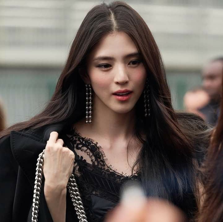 a woman with long dark hair wearing black clothes and holding a chain around her neck