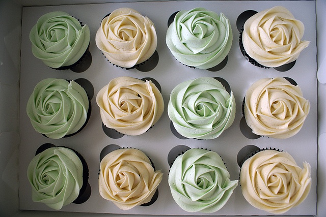 twelve cupcakes with green and yellow frosting in a white box on a table