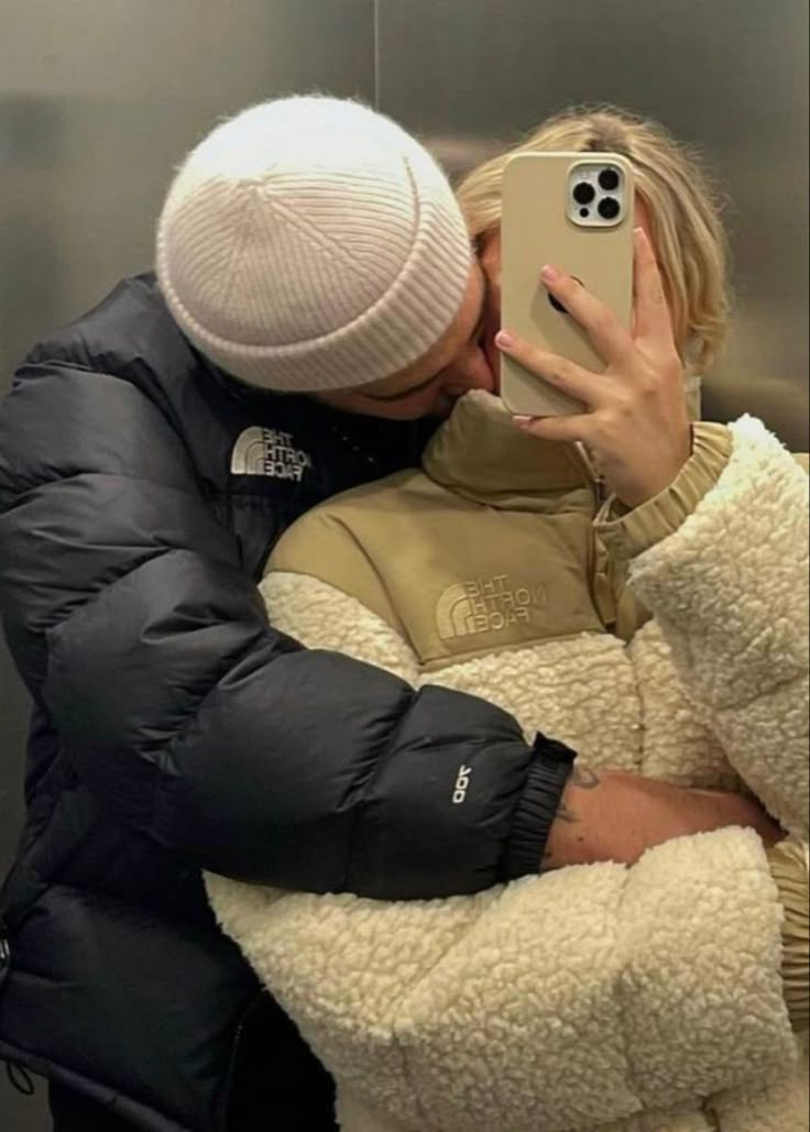 a woman taking a selfie with her cell phone while wearing a winter coat and hat